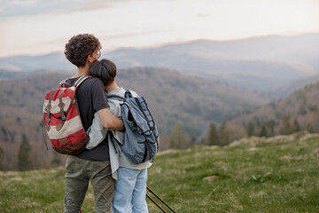 Rear on young couple in hugs watching amazing view from peak of mountains. At wild nature.