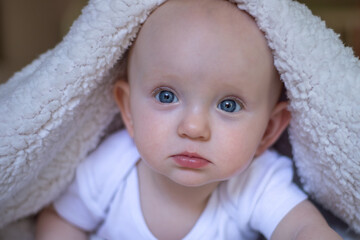 smiling baby looking at camera under a white blanket, towel. selective focus