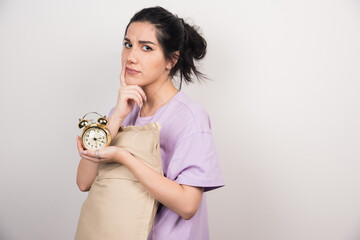 Young woman holding alarm clock and cushion on white background