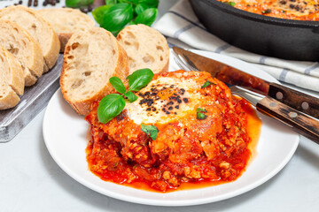 Shakshuka with eggs, Italian sausage, tomato sauce, on a white plate, horizontal