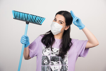 Woman posing with medical facemask and broom on white background