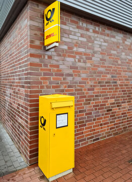 Kiel, Germany - 07. July 2022. A yellow german postbox at a red brick wall with a german post sign above it.