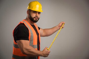 Engineer in orange uniform and yellow helmet using ruler