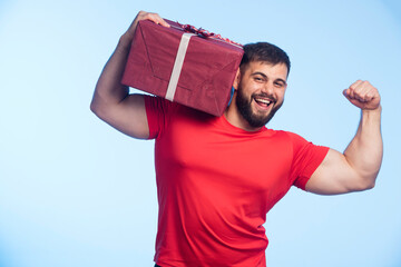 Man in red shirt holding gift box in the shoulder and showing muscles