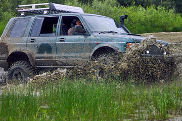 SUV or off-road vehicle crosses a river with splashes of dirty water. Extreme, challenging track...