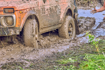 Fototapeta na wymiar Off road car on bad road. Expedition in four-wheel drive orange car to the village on mountain road. Splashes of mud and water during racing. Wheel is slipping. Powerful male hand supports participant