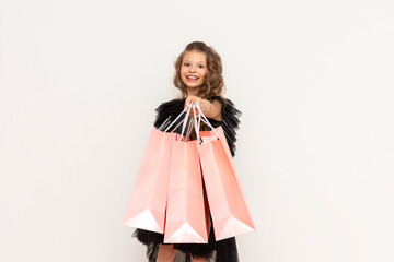 A joyful girl in a dress holds a shopping bag on Black Friday. Shopping for a little princess with curly hair on a white isolated background.