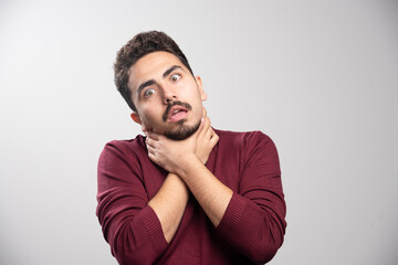 A young brunette man strangling himself over a gray wall