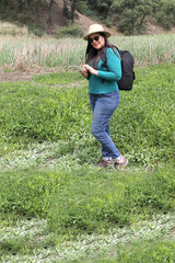 Latin adult woman with hat and sunglasses is in the middle of the forest using his cell phone to send and receive messages and search the location on the map