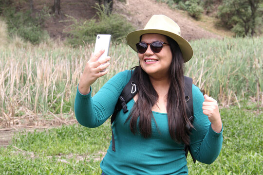 Latin adult woman with hat and sunglasses is in the middle of the forest using his cell phone to send and receive messages and search the location on the map