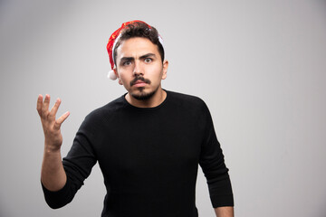 Naklejka premium Disgruntled man wearing Santa Claus red hat over a gray wall