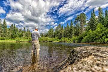 Fototapeta na wymiar A man wading in the shallow water of a river fishing 