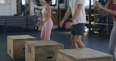 Group of fit people exercising and jumping on wooden boxes during a HIIT fitness class with a trainer. Diverse team of active, athletic, sweaty man and women performing cardio training and workout