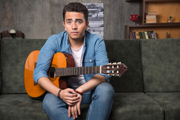 Young guitar player holding a beautiful guitar and sitting on sofa