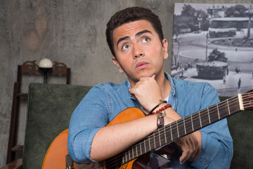 Obraz premium Thoughtful musician holding a beautiful guitar and sitting on sofa