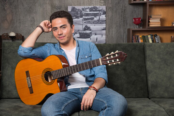 Young guitar player holding a beautiful guitar and sitting on sofa