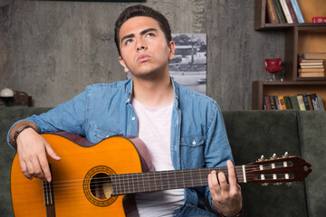 Young musician holding a beautiful guitar and sitting on sofa
