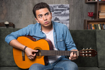 Young musician playing guitar and sitting on sofa