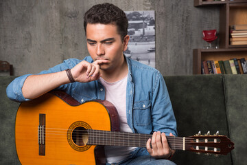 Young musician holding a beautiful guitar and sitting on sofa