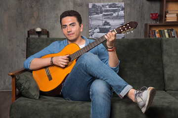 Smiling musician playing the guitar and sitting on sofa