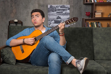 Serious musician holding a beautiful guitar and sitting on sofa