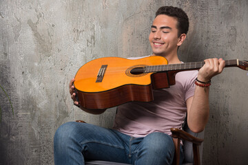 Smiling musician looking on guitar on marble background