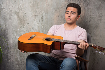 Young musician looking on guitar on marble background