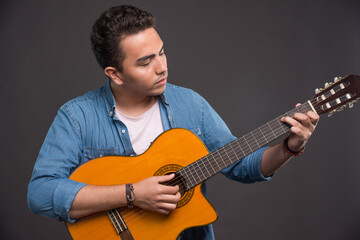 Young musician playing guitar on black background
