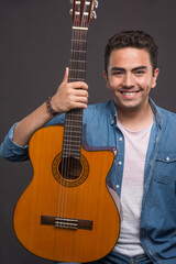 Positive man holding a beautiful guitar on black background