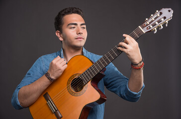 Young man playing with guitar on dark background