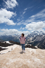 Obraz premium Cute teen girl in a pink jacket blue jeans and white sneakers standing on top of the mountains