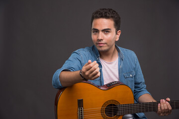 Young man with guitar posing on dark background