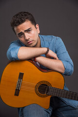 Tired young man with guitar sitting on dark background