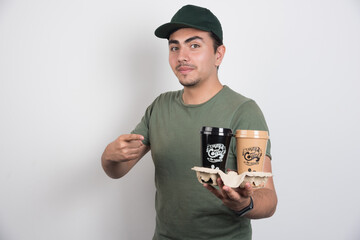 Courier pointing at takeaway cups of coffees on white background