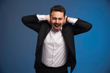 Fototapeta premium Businessman in black suit covering her ears and screaming