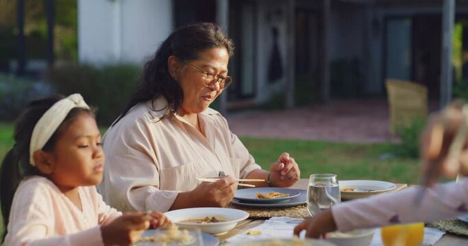 Happy family eating together at a table outside in their backyard. Asian grandmother and child sitting together and having lunch or dinner at an outdoor dining area. Having fun and enjoying good food