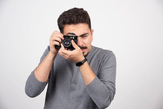 Young man taking pictures with camera on white background