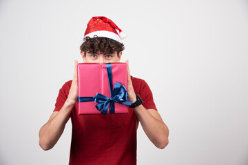 Fototapeta na wymiar Young male in Santa hat hiding behind gift box