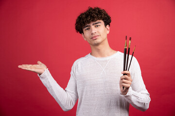 Young painter with brush standing on red background