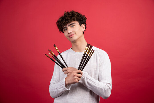 Male artist with brushes posing on red background