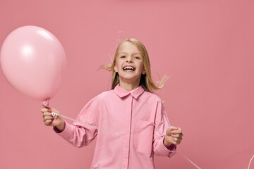 sweet, pleasant, radiant girl, blonde, stands with a pink balloon in her hand and smiles joyfully looking at the camera