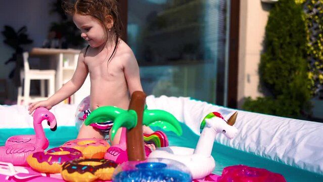 little baby girl having fun, playing with toys in an inflatable pool at summer patio at home