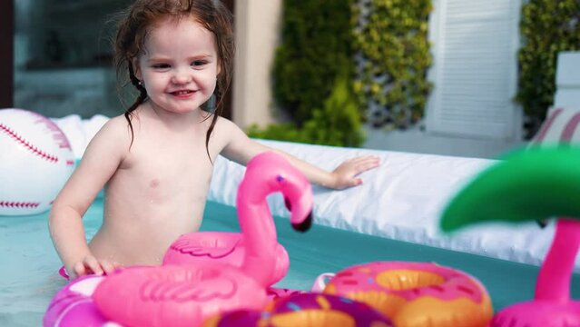 little baby girl having fun, playing with toys in an inflatable pool at summer patio at home