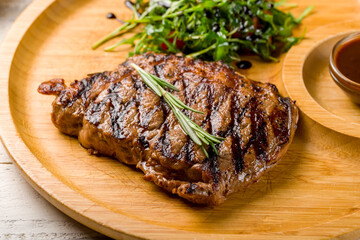 juicy Ribeye steak on wooden plate with aragula, tomatoes and pepper sauce macro close up