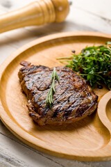 juicy Ribeye steak on wooden plate with aragula, tomatoes and pepper sauce vertical macro close up