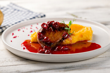 Duck breast with berry sauce and mashed potatoes on white plate on white wooden table macro close up