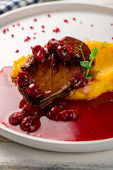 Duck breast with berry sauce and mashed potatoes on white plate on white wooden table macro close up vertical