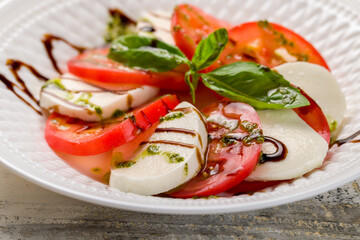 Caprese salad with mozzarella and tomato with basil and balsamic and pesto sauce on white plate macro close up