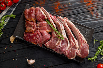 raw lamb on dark plate, rack of lamb and lamb meat top view on black wooden table