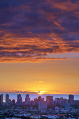 Obraz premium A sunset over a city skyline near the sea with cloudy purple and orange sky. Sunrise over a blue horizon near urban landscape with copy space. Peaceful holiday destination at night in Waikiki, Hawaii